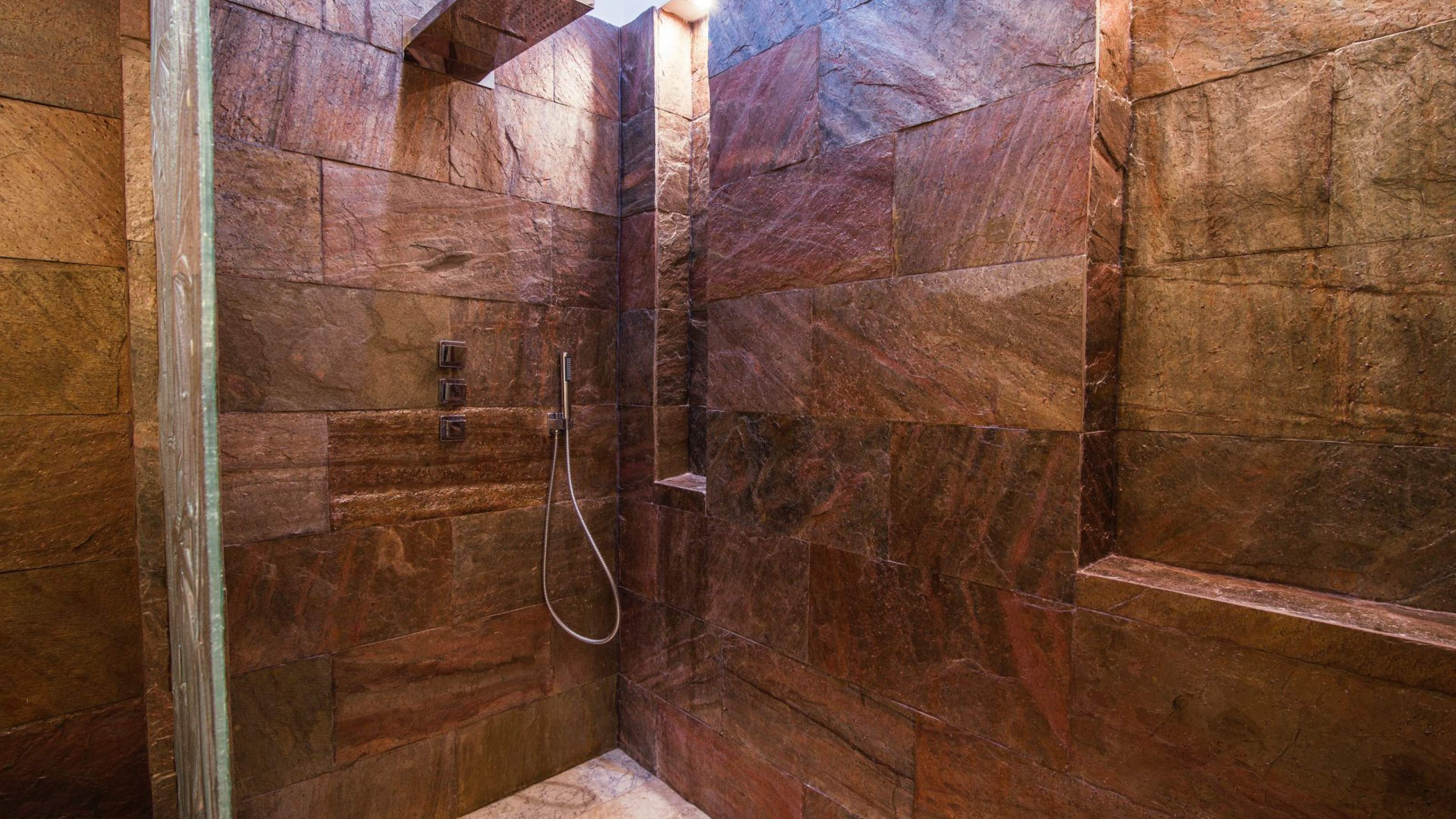 Masowa Stone - Stone Veneer Experts, UK-wide from Arbroath. Modern shower area with dark stone tiles, built-in niches, and a handheld showerhead attached to the wall.