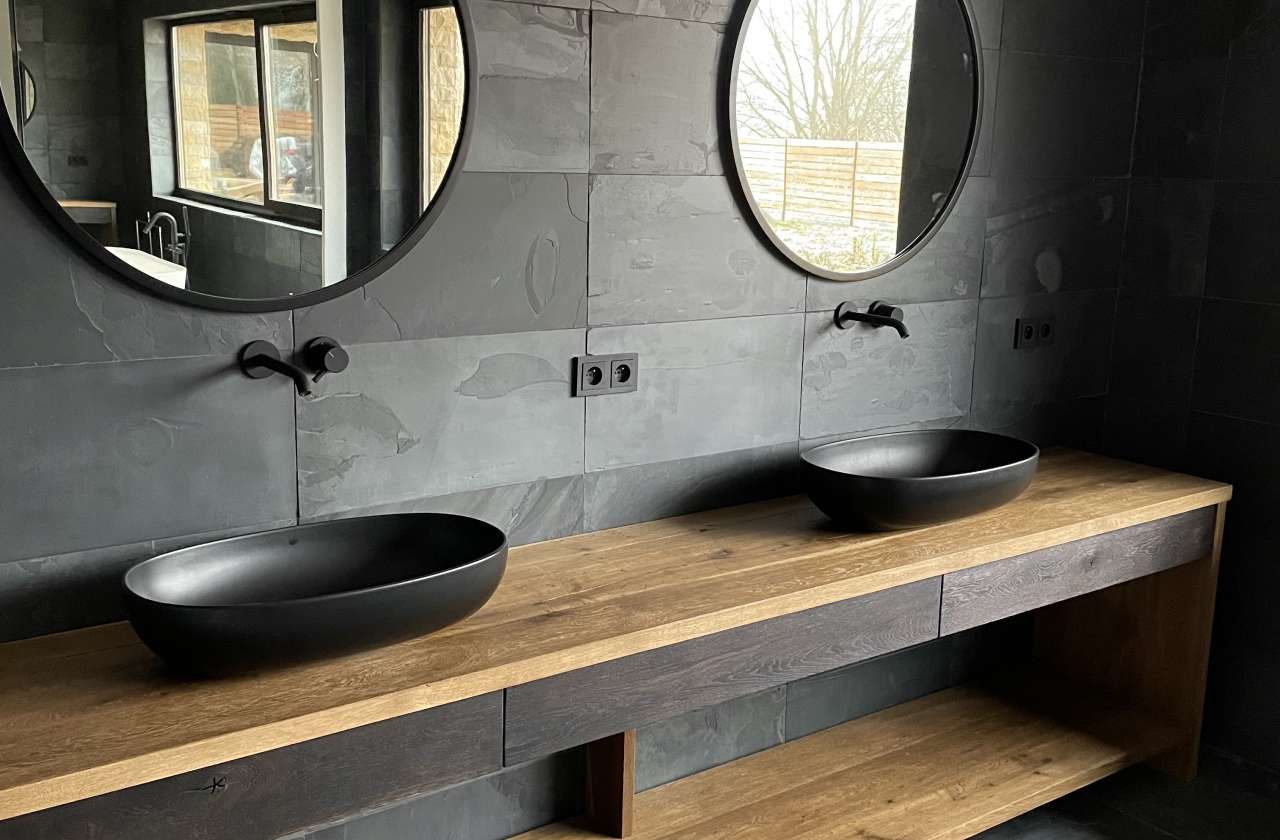 Masowa Stone - Stone Veneer Experts, UK-wide from Arbroath. Modern bathroom with two black oval sinks on a wooden countertop and round mirrors above each sink.